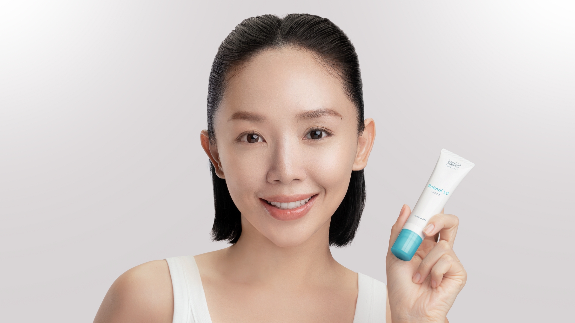 Obagi - ca sĩ Tóc Tiên mặc áo tank top màu trắng, buộc tóc nửa đầu, tay cầm tuýp kem dưỡng retinol của Obagi và nhìn chính diện vào camera để chụp ảnh chân dung