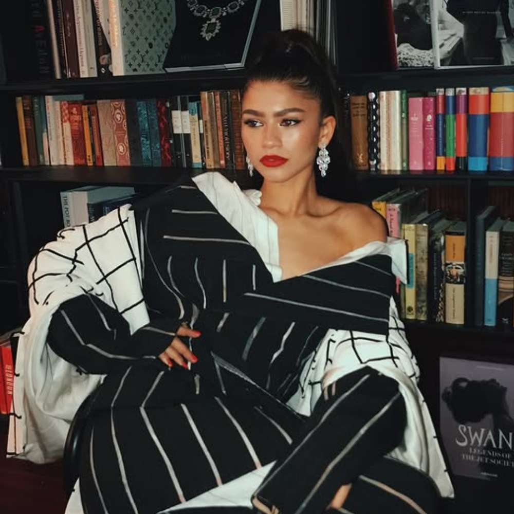 Zendaya cột tóc cao và tạo dáng đứng trước kệ sách