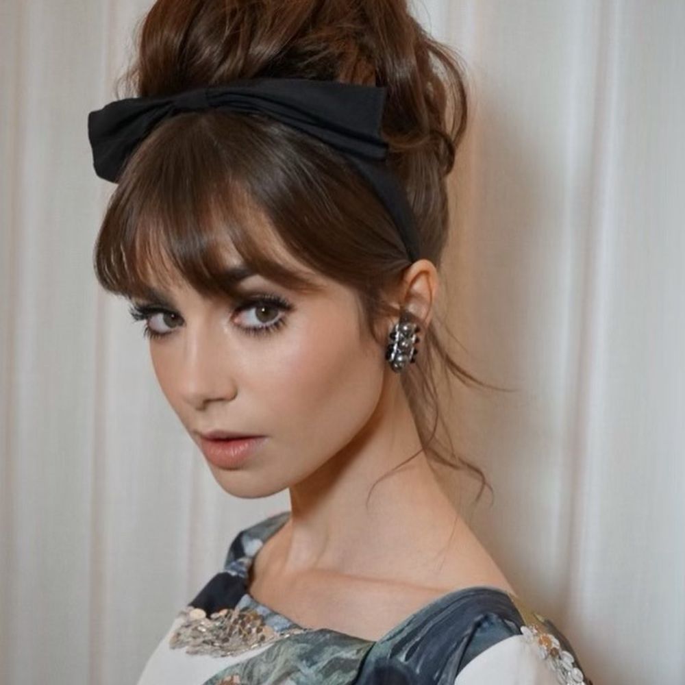 Hình ảnh Lily Collins với tóc búi cổ điển và băng đô nơ đen.