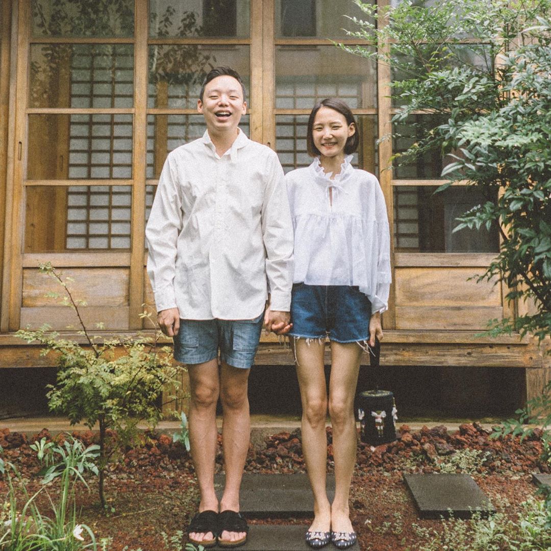 Cặp đôi mặc sơ mi trắng và quần shorts jeans chụp ảnh trước hiên nhà