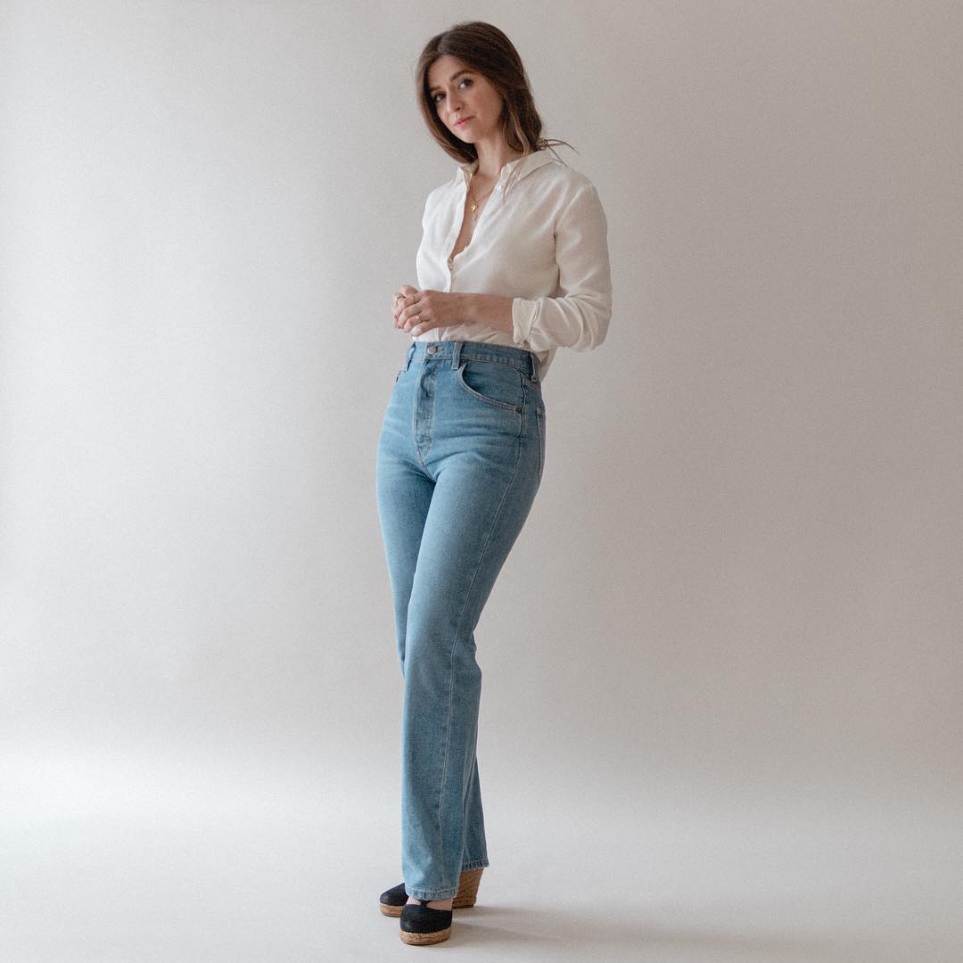 Cô gái mặc quần jeans ống loe, áo sơ mi trắng, mang giày đế xuồng