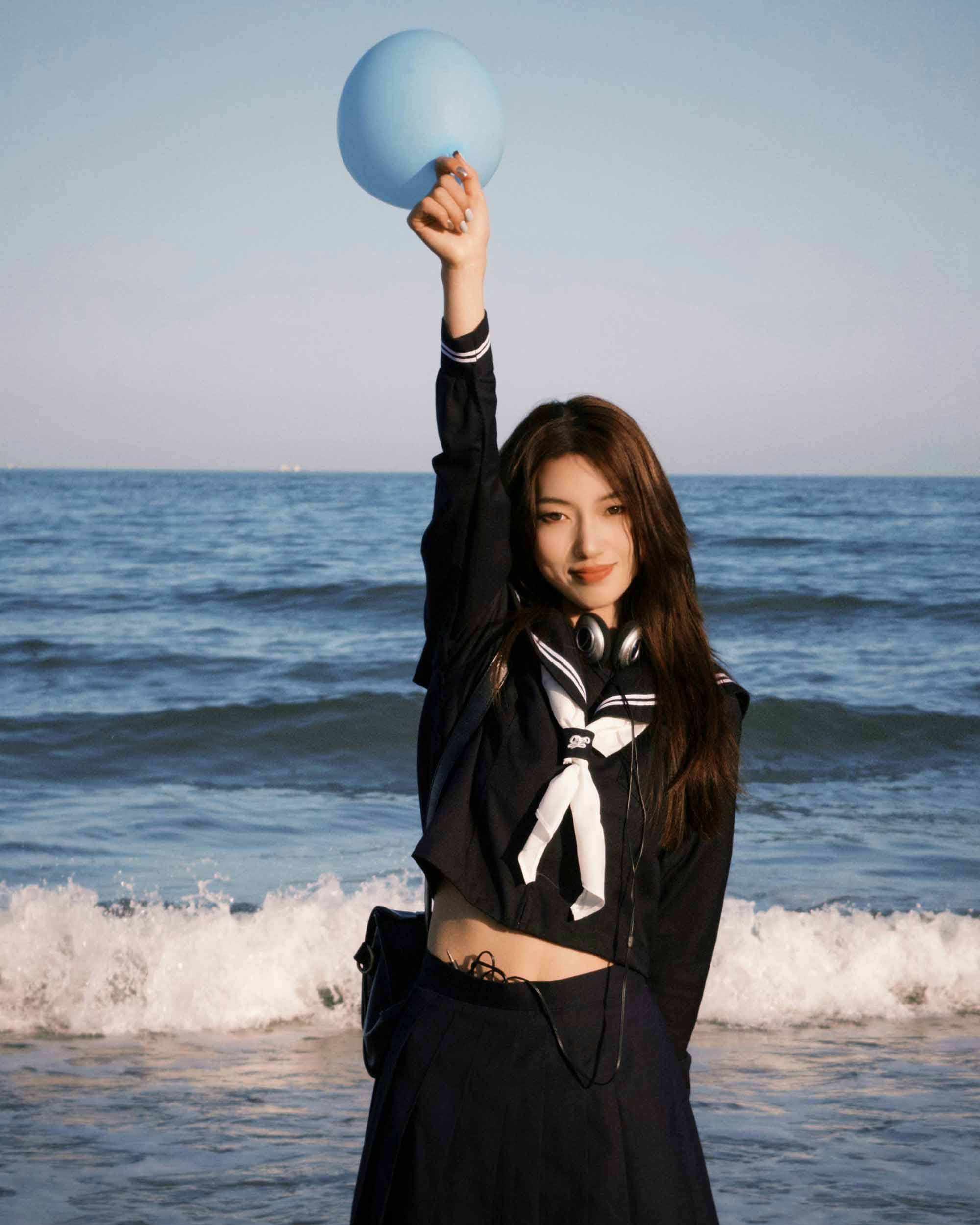 cô gái mặc đồng phục học sinh cầm bóng bay bên bờ biển