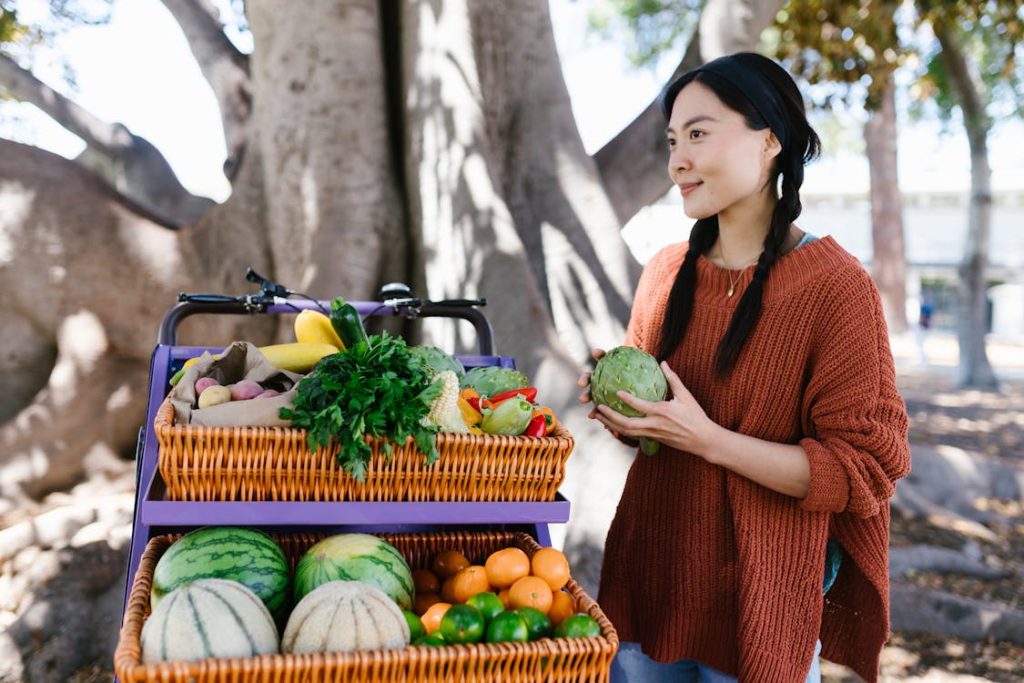 Cô gái đang cầm bông atiso đứng bên giỏ rau củ quả