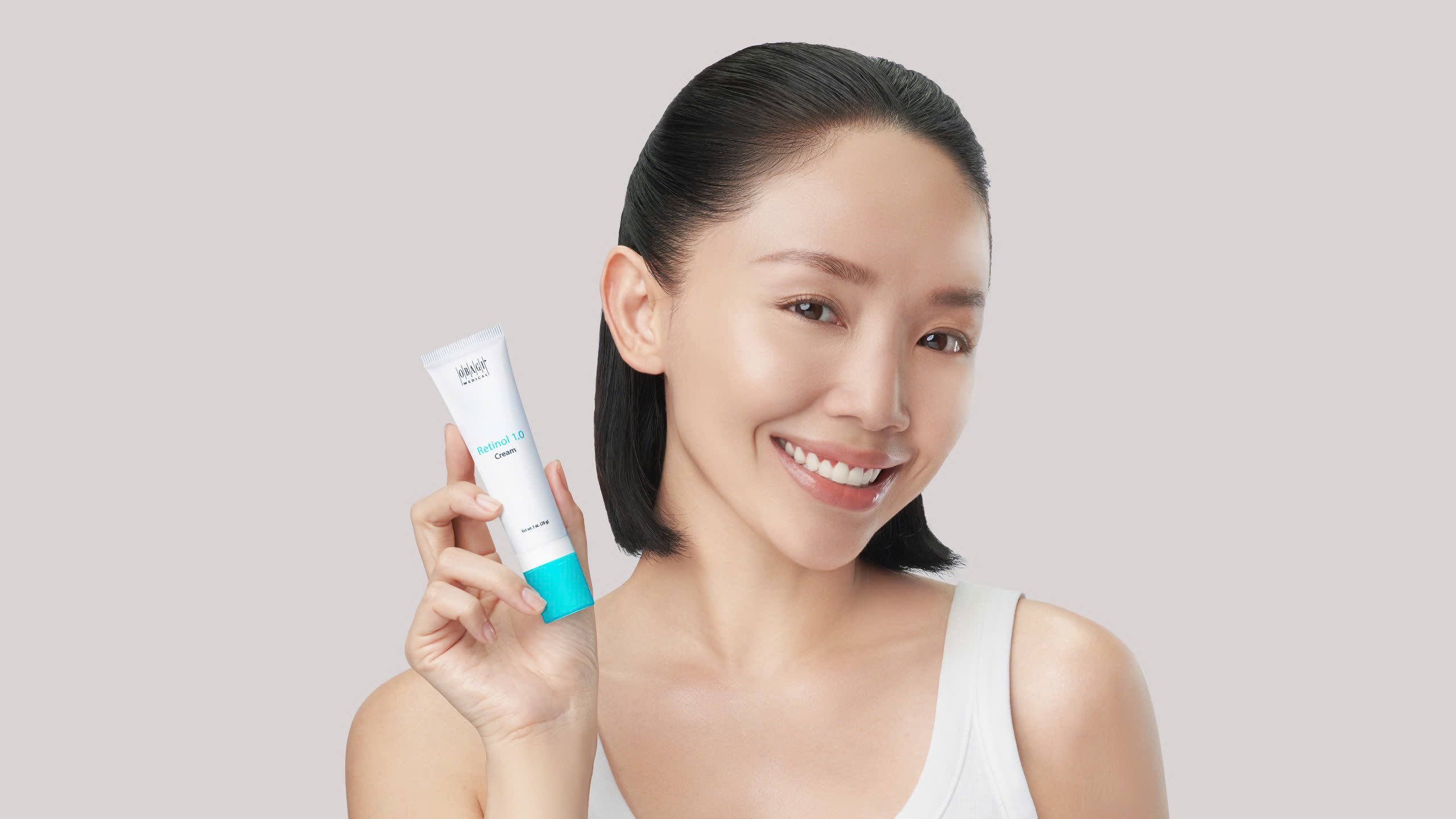 Obagi - ca sĩ Tóc Tiên mặc áo tank top màu trắng, buộc tóc nửa đầu và tay cầm tuýp kem dưỡng retinol của Obagi