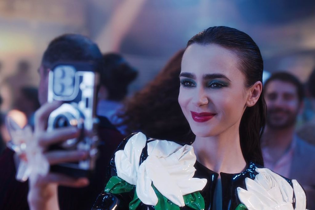 emily in paris - Lily Collins buộc tóc đuôi ngựa, trang điểm đậm và cầm điện thoại selfie