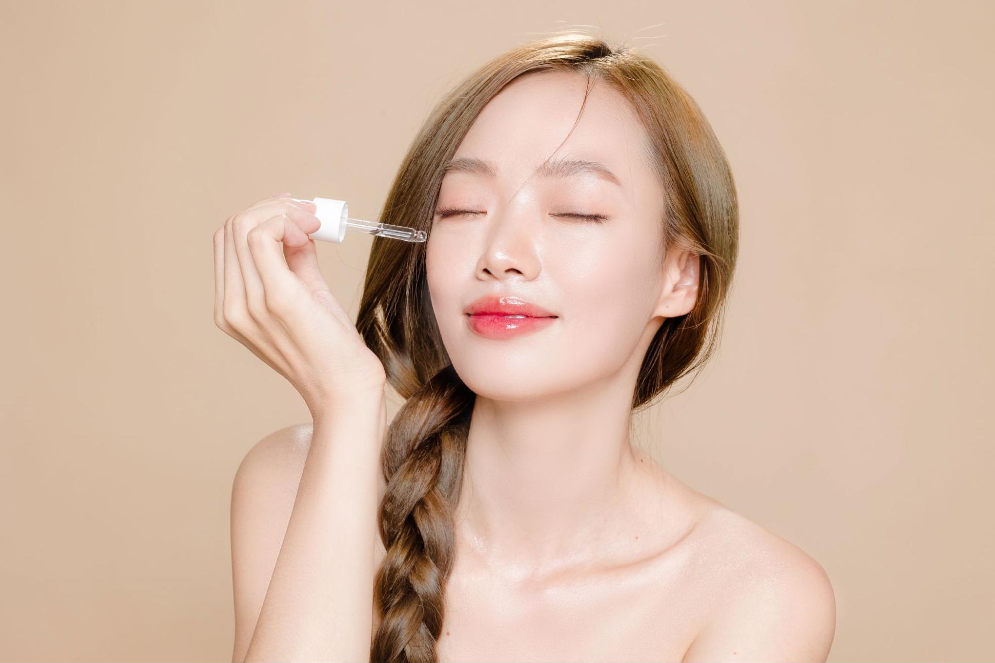 tế bào gốc - cô gái châu Á thắt bím một bên và dùng tay bôi serum