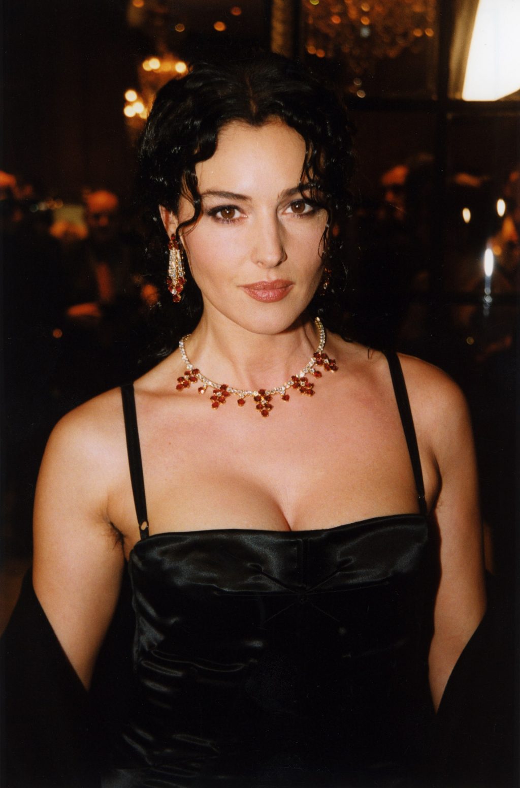 Monica Bellucci mặc đầm hai dây màu đen, đeo dây chuyền màu đỏ và tạo kiểu búi tóc cao để chụp ảnh chân dung