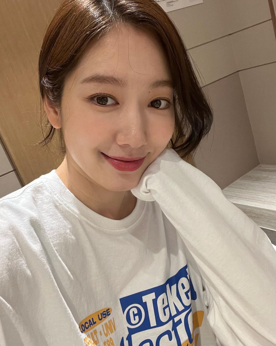 skincare - diễn viên Park Shin Hye mặc áo sweater màu trắng, búi tóc cao và tạo dáng chống cằm để selfie